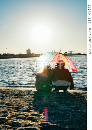 A boy and a girl sharing a colorful umbrella under the sunlight of the seaside sunset A boy and a girl sharing a colorful umbrella under the sunlight of the seaside sunset 118441465