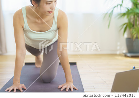 A young woman taking an online yoga class at home and posing 118442015