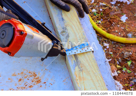 In process of framing new house, air pneumatic hammers are used to nail wooden beams to concrete 118444078