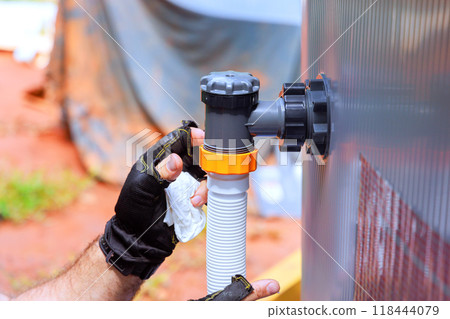 An employee of an environmental maintenance company installs water filtration system, chlorination system for swimming pool frame 118444079