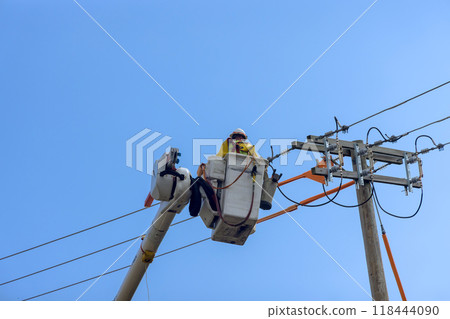 In order to maintain service at high voltage power line, an electrician officer uses insulated crane basket while working on climbing pole 118444090
