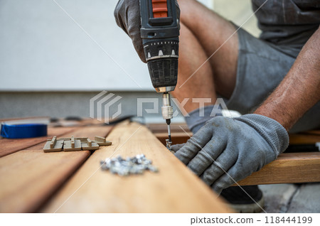 Worker wearing protective gloves fixating wooden plank for outside patio 118444199
