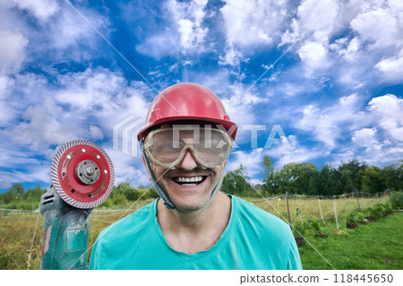 Crazy smile of an eccentric worker who is demonstrating red circular saw. Crazy smile of an eccentric worker who is demonstrating red circular saw. 118445650