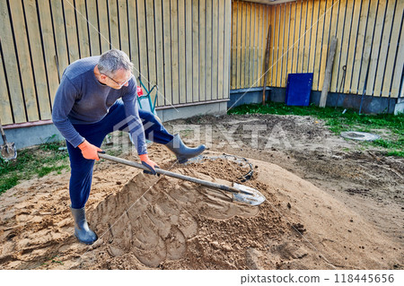 Construction worker slaps shovel on pile of sand around perimeter of septic tank manhole to compact it. Construction worker slaps shovel on pile of sand around perimeter of septic tank manhole to compact it. 118445656