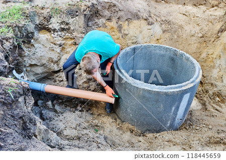 Plumber marks hole for inlet pipe in concrete ring of septic tank. 118445659
