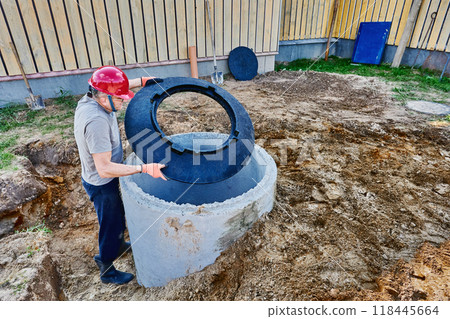 Worker installs base of manhole cover on septic tank made of concrete rings. 118445664