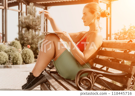 Woman, Bench, Park - A woman wearing a red tank top and green shorts sits on a wooden bench in a park and reads a book. Woman, Bench, Park - A woman wearing a red tank top and green shorts sits on a wooden bench in a park and reads a book. 118445716