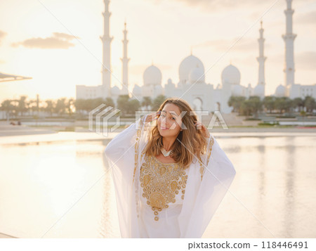 Travel to the United Arab Emirates, Abu Dhabi. Woman in white Arabic dress looking at Sheikh Zayed Great white mosque. famous Abu Dhabi sightseeing. Travel to the United Arab Emirates, Abu Dhabi. Woman in white Arabic dress looking at Sheikh Zayed Great white mosque. famous Abu Dhabi sightseeing. 118446491
