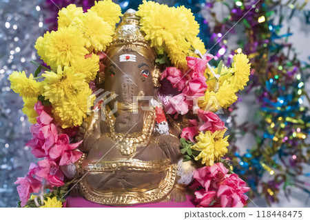 Hindu god Ganesha statue made of clay decorated with flower garlands on bokeh effect background. Closeup Hindu god Ganesha statue made of clay decorated with flower garlands on bokeh effect background. Closeup 118448475