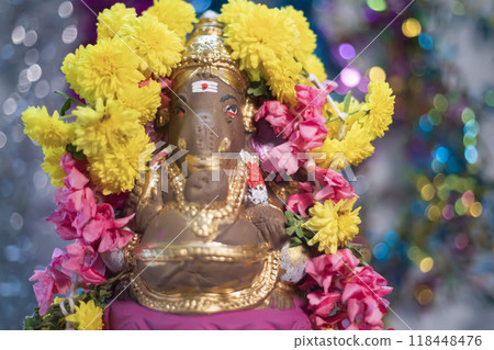 Hindu god Ganesha statue made of clay decorated with flower garlands on bokeh effect background. Closeup Hindu god Ganesha statue made of clay decorated with flower garlands on bokeh effect background. Closeup 118448476