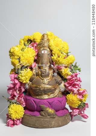 Hindu god Ganesha idol made of clay decorated with flower garlands on white background. Hindu god Ganesha idol made of clay decorated with flower garlands on white background. 118448480