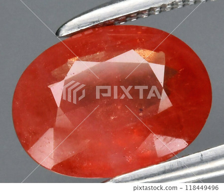 Stunning Close-Up of a Vibrant Oval-Cut Orange Gemstone Held by Precision Tweezers Against a Plain Background Stunning Close-Up of a Vibrant Oval-Cut Orange Gemstone Held by Precision Tweezers Against a Plain Background 118449496