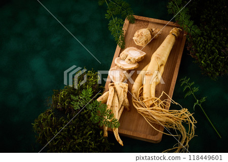 Ginseng Root on a wooden tray with green foliage background. 118449601