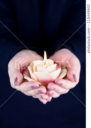 Lit rose-shaped candle in female hands with fashionable manicure. 118449602