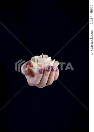 Female hand holding a lit candle in the shape of a rose. Female hand holding a lit candle in the shape of a rose. 118449603