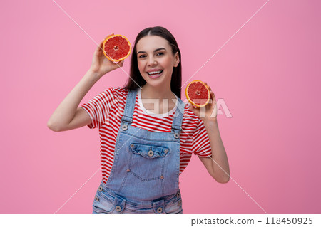 Cute smiling young woman holding slices of grapefruit in hands Cute smiling young woman holding slices of grapefruit in hands 118450925