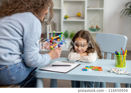 Cute girl sitting at the table while having a speech therapy tutorial and smiling nicely 118450956