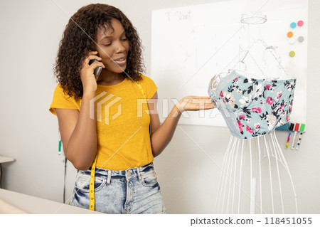 Curly-haired female dressmaker standing near dummy with a new model on it 118451055