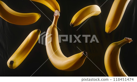 Ripe bananas are seen floating effortlessly against a dark background, highlighting their bright yellow color and curved shape. The arrangement captures a sense of motion and whimsy 118451474
