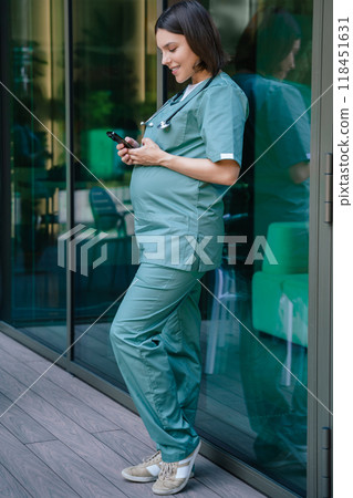 Pregnant young woman in lab coat standing and holding a phone in hands 118451631