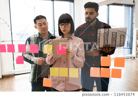 Team brainstorming with sticky notes and digital devices in modern office Team brainstorming with sticky notes and digital devices in modern office 118453874