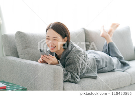 A woman in her 40s looking at her smartphone on the sofa A woman in her 40s looking at her smartphone on the sofa 118453895