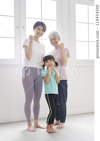 Portrait of three generations of women wearing sportswear and posing with fist pumps, full body 118454500