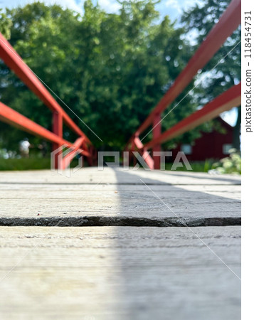 The empty wooden brown bridge top with blur background of green tree, red railing and blue sky. Exuberant image. 118454731