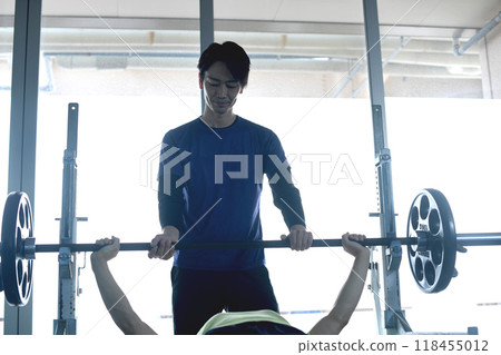Male instructor assisting a man doing bench press in personal training at the gym Male instructor assisting a man doing bench press in personal training at the gym 118455012