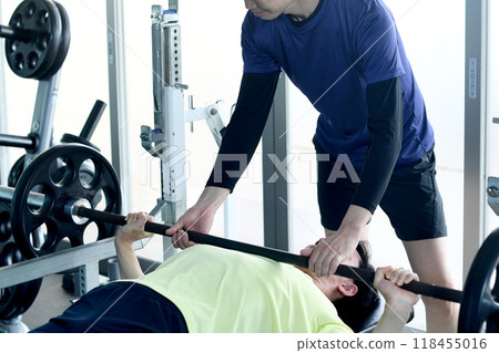 Male instructor assisting a man doing bench press in personal training at the gym 118455016