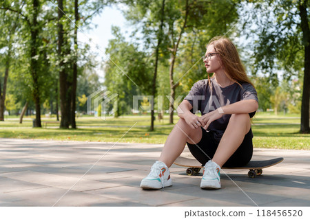 Easygoing portrait highlighting a young female's confident poise as she sits atop a skateboard, representing the independent, athletic nature of modern youth culture 118456520