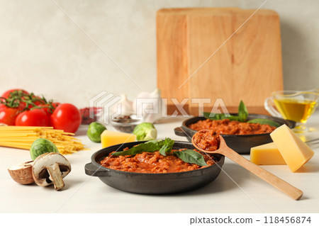 Pans with Bolognese sauce, wooden spoon and ingredients on light background Pans with Bolognese sauce, wooden spoon and ingredients on light background 118456874