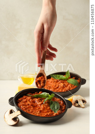 Pans with Bolognese sauce, ingredients and wooden spoon in hand on light background Pans with Bolognese sauce, ingredients and wooden spoon in hand on light background 118456875
