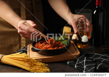 Bolognese sauce, bottle of oil and wooden spoon in hands, cheese and spaghetti on dark background Bolognese sauce, bottle of oil and wooden spoon in hands, cheese and spaghetti on dark background 118456877
