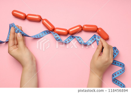 Small sausages with a measuring tape on a pink background Small sausages with a measuring tape on a pink background 118456894