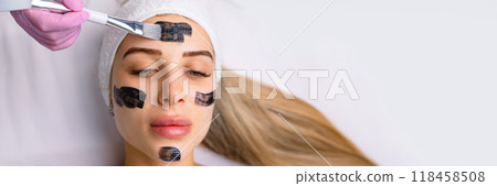 cosmetologist applying black mask on pretty woman face wearing black gloves, gorgeous woman in spa having facial procedures cosmetologist applying black mask on pretty woman face wearing black gloves, gorgeous woman in spa having facial procedures 118458508