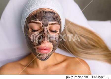 cosmetologist applying black mask on pretty woman face wearing black gloves, gorgeous woman in spa having facial procedures cosmetologist applying black mask on pretty woman face wearing black gloves, gorgeous woman in spa having facial procedures 118458509