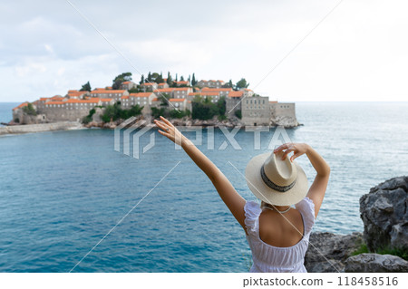 girl tourist in a hat looks from a top on the island of Sveti Stefan in Montenegro and the sea 118458516