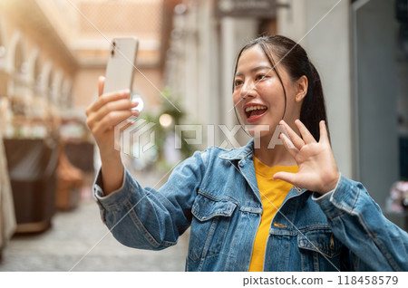 A charming Asian woman is talking on a video call with a smartphone while strolling through the city 118458579