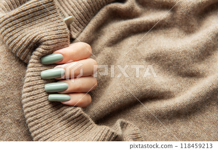 Elegant hand with long green nails holding a textured beige sweater during autumn fashion season 118459213