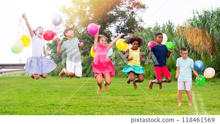 Cheerful tween girls and boys with balloons in hands jumping in summer park 118461569