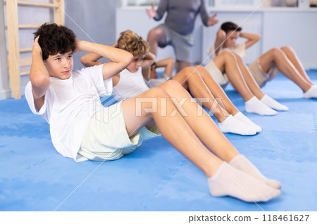 Teenagers performing sit-ups during training under guidance of coach 118461627