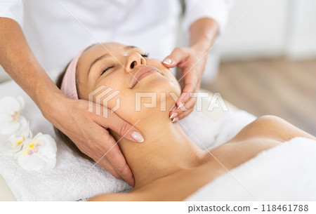 Young woman client gets procedure of rejuvenating massage face skin on cosmetologist visit Young woman client gets procedure of rejuvenating massage face skin on cosmetologist visit 118461788