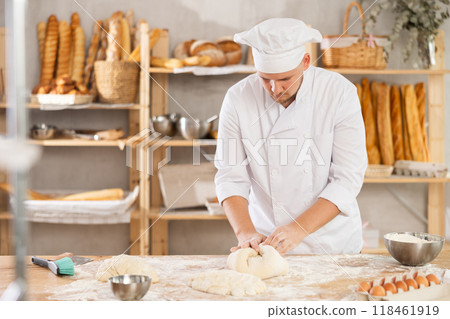 Guy works in bakery as baker, kneads dough, works with flour. 118461919