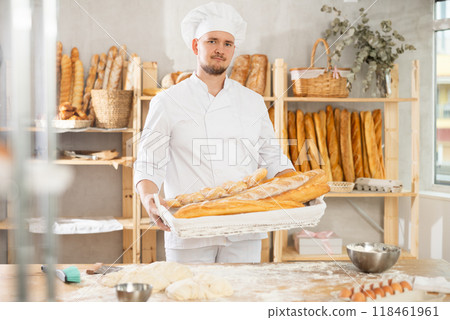 Male baker holds basket with finished products, shows many different baguettes Male baker holds basket with finished products, shows many different baguettes 118461961