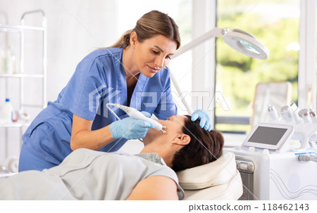 Female aesthetician performing radiofrequency facial skin tightening procedure on mature woman 118462143