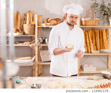Professional baker stands at his work bench, kneading and shaping dough to make bread and baguettes 118462176