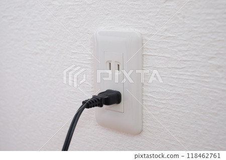 An electrical outlet and plug on a plaster wall 118462761