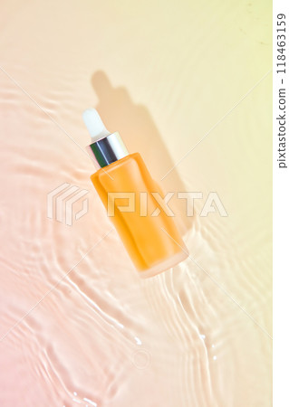 A glass bottle filled with a liquid sits on a water ripple and gradient surface of pink and orange. This image creates a dreamy atmosphere, ideal for promoting skincare products. A glass bottle filled with a liquid sits on a water ripple and gradient surface of pink and orange. This image creates a dreamy atmosphere, ideal for promoting skincare products. 118463159