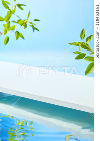 The photo features a white surface on a blue water pool of blue water, surrounded by green leaves from top of frame, with a summer atmosphere, ideal for promoting beauty products. The photo features a white surface on a blue water pool of blue water, surrounded by green leaves from top of frame, with a summer atmosphere, ideal for promoting beauty products. 118463161